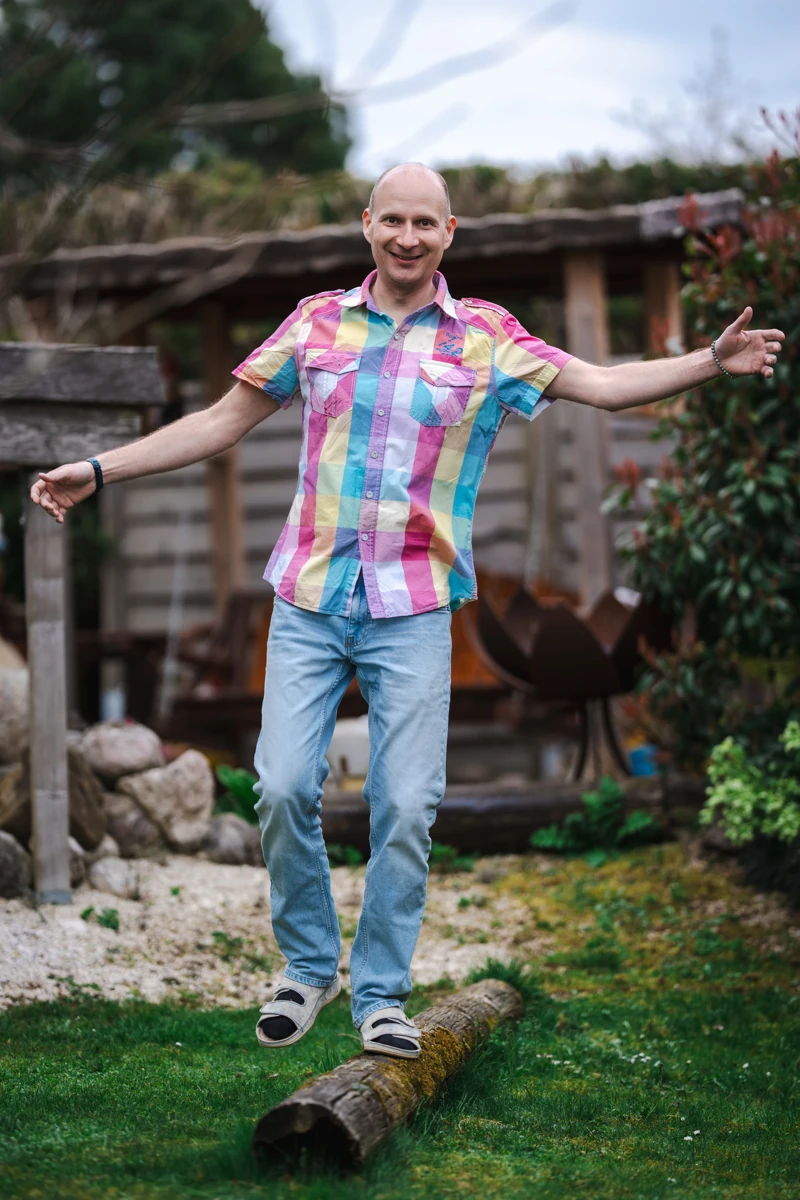 Ronald im Garten, mit offenen Armen auf einem Baumstamm balancierend
